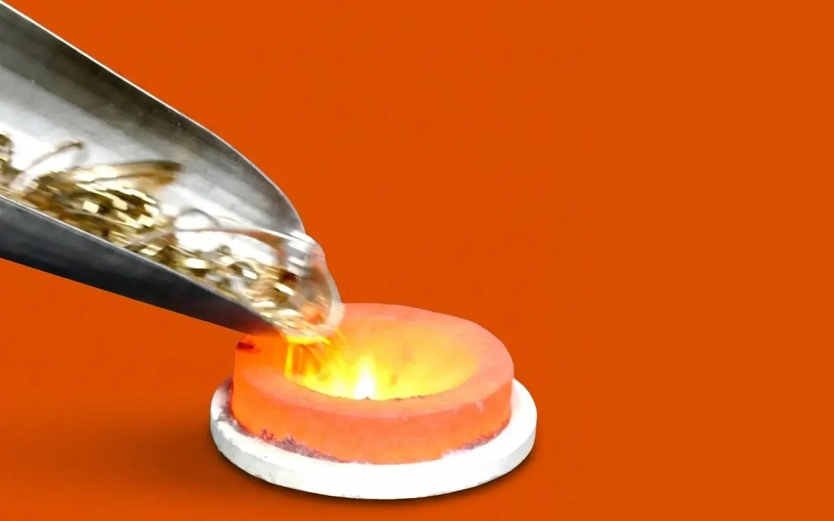 Goldschmuck wird aus einer Metallschaufel in einen glühend heißen Schmelztiegel geschüttet, um für das Recycling eingeschmolzen zu werden.