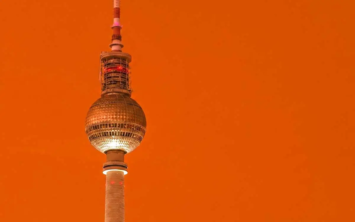 Eine minimalistische Grafik des Berliner Fernsehturms vor einem orangen Hintergrund.