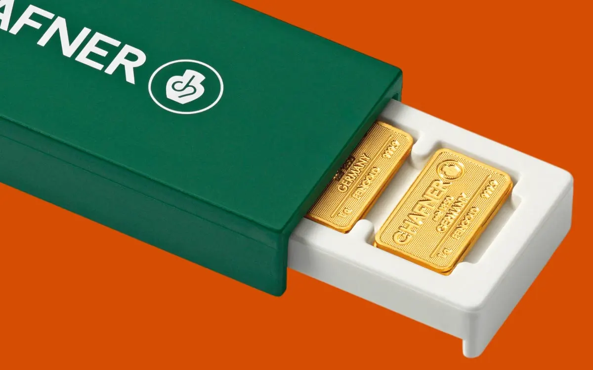 Mehrere kleine Goldbarren von C. Hafner, sicher verpackt in einer grünen Blisterkarte (SmartCard), liegen auf einer orangefarbenen Fläche.