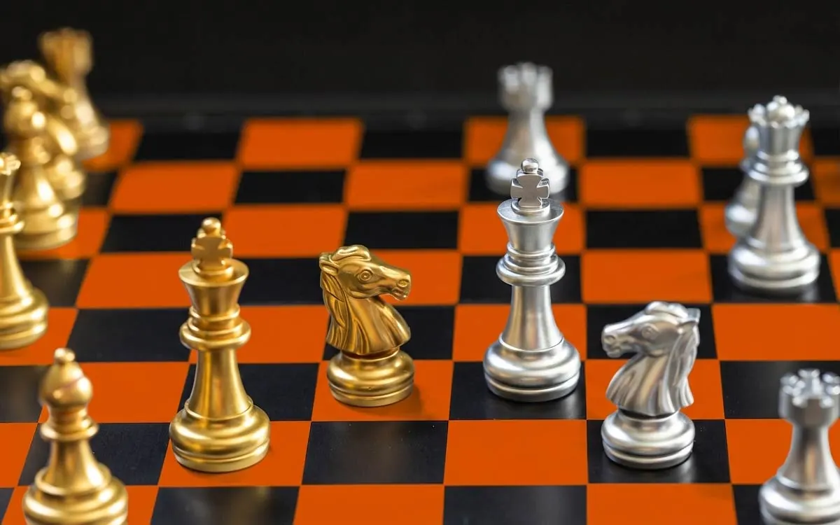 Goldene und silberne Schachfiguren auf einem modern gestalteten Schachbrett in den Farben Schwarz und Apex-Orange. Metapher für kluge Anlagestrategien und die Diversifikation zwischen Gold und Silber.