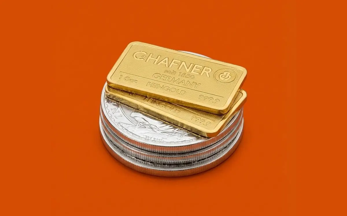 Zwei 1-Unzen-Goldbarren von C. Hafner liegen gestapelt auf einem Turm aus Silbermünzen vor einem kräftigen orangefarbenen Hintergrund.