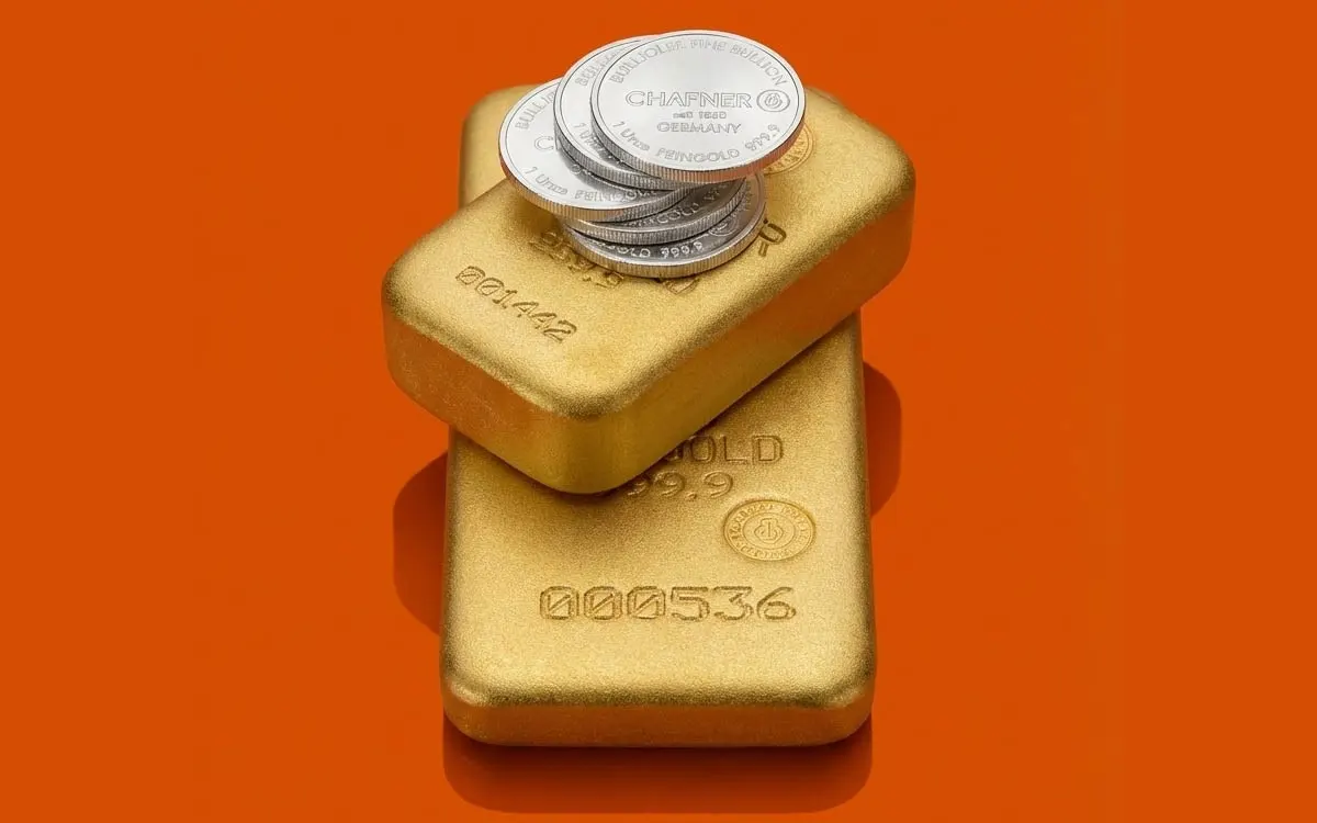 Stapel aus zwei gegossenen Goldbarren mit aufgelegten Silbermünzen auf einem Hintergrund in Apex-Orange. Symbolbild für den Kauf von Edelmetallen und die Kombination verschiedener Anlageklassen zur Vermögenssicherung.