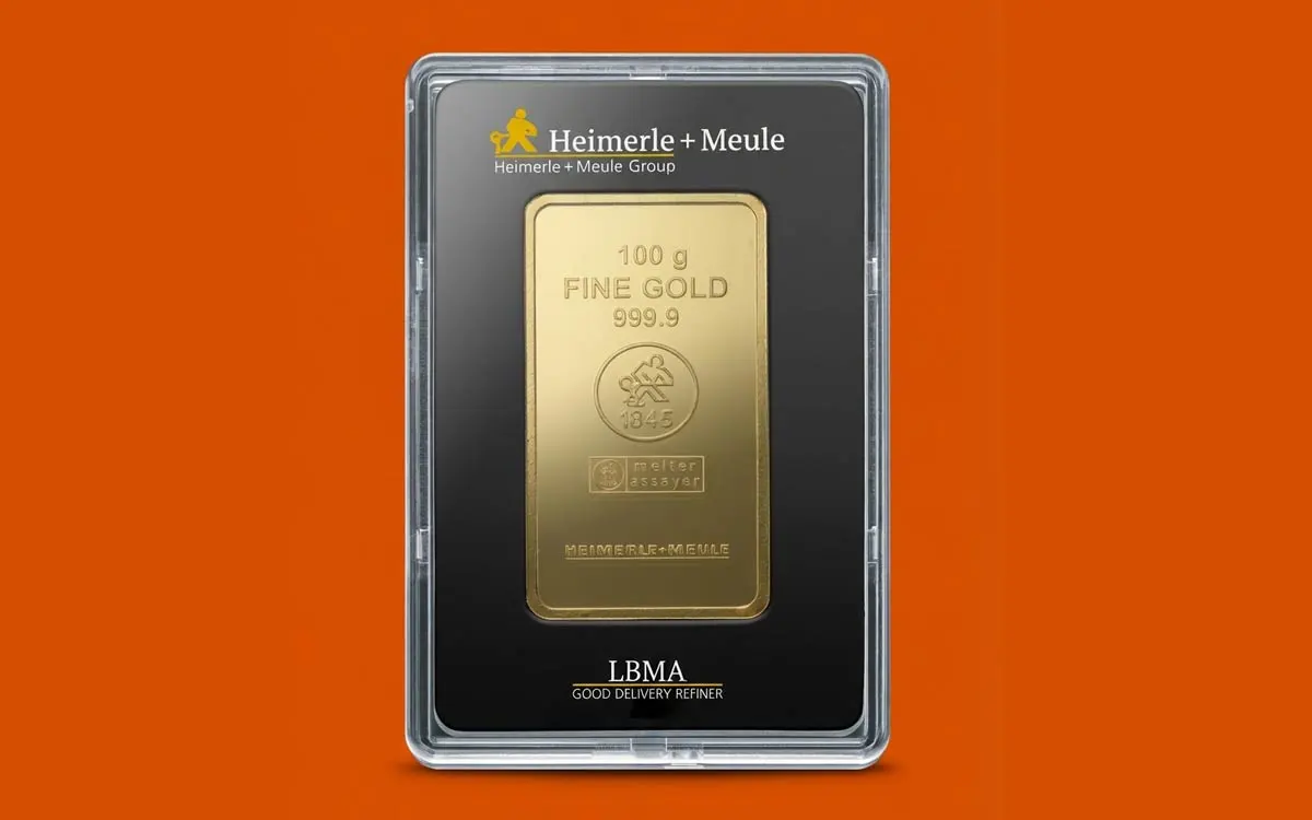 Ein 100 Gramm Feingoldbarren (999.9) von Heimerle + Meule in einer schwarzen Sicherheits-Blisterkarte mit "LBMA Good Delivery Refiner"-Zertifizierung, freigestellt auf Apex-Orange. Hochwertiges Anlagegold zur Vermögenssicherung.